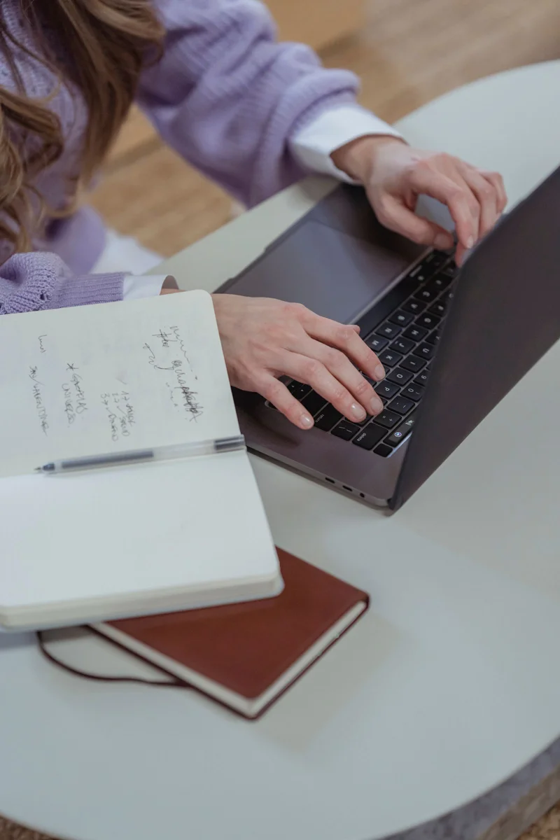 Une personne suit une formation sur ordinateur portable, un carnet de notes ouvert à côté.