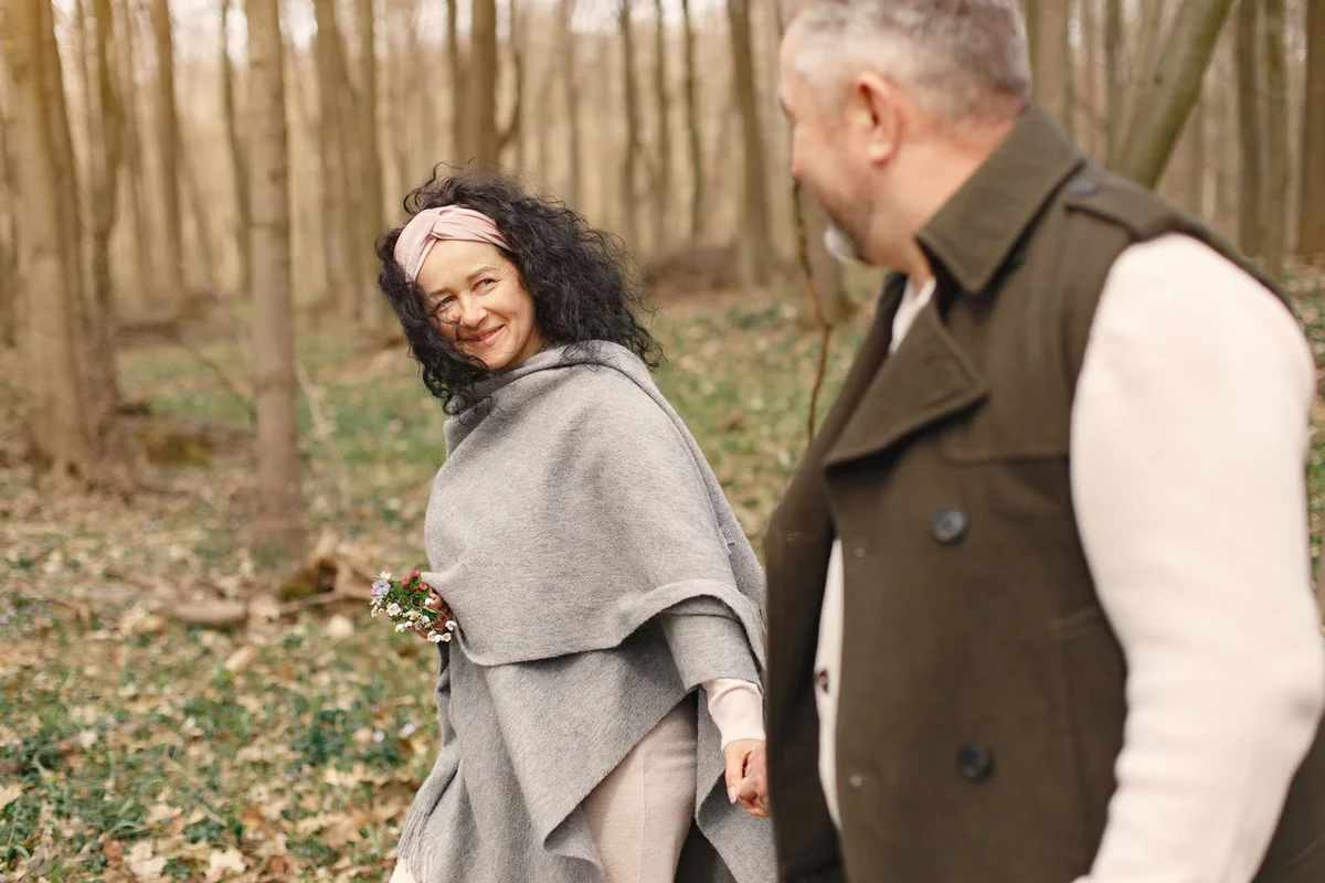 Un couple marche main dans la main dans une forêt de printemps, la femme sourit en se retournant.
